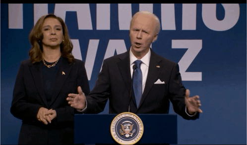 A Man In A Suit And Tie Stands At A Podium With A Woman Behind Him In Front Of A Sign That Says Vaz GIF