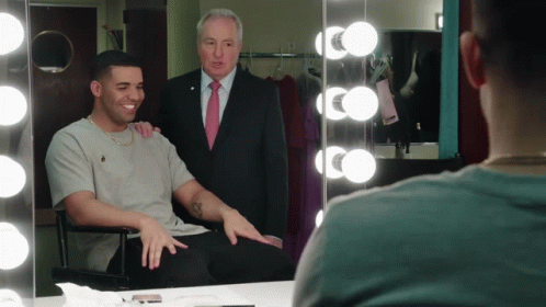 A Man In A Suit And Tie Stands Behind A Man In A Chair GIF