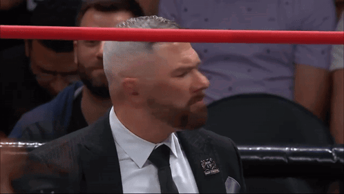 A Man In A Suit And Tie Stands In A Boxing Ring With A Red Rope GIF