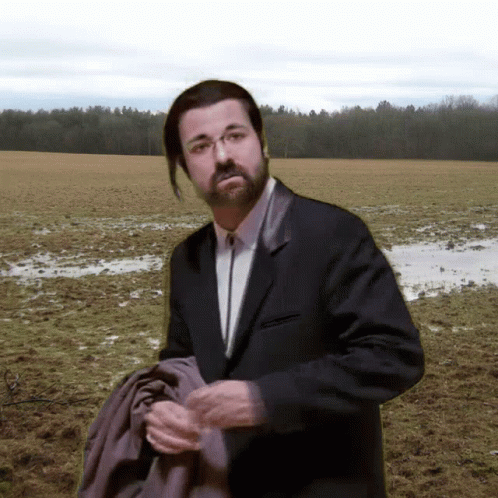 A Man In A Suit And Tie Stands In A Field GIF