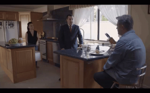 A Man In A Suit And Tie Stands In A Kitchen Talking To A Woman GIF