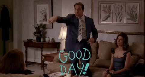 A Man In A Suit And Tie Stands In A Living Room With The Words Good Day Written On The Wall GIF