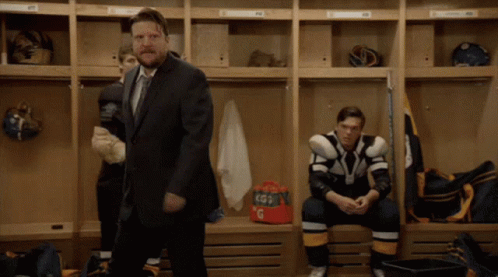A Man In A Suit And Tie Stands In A Locker Room GIF