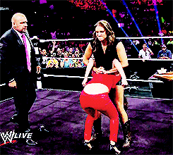 A Man In A Suit And Tie Stands In A Wrestling Ring Watching A Woman In Red Tights GIF
