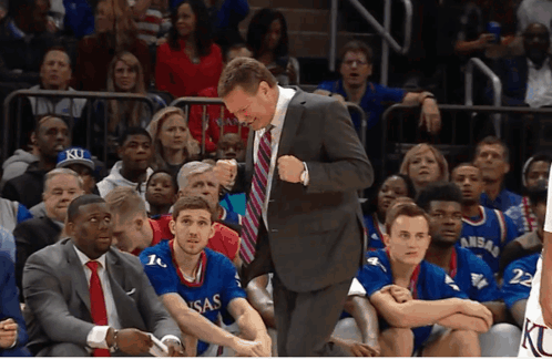 A Man In A Suit And Tie Stands In Front Of A Basketball Team Wearing Kansas Jerseys GIF