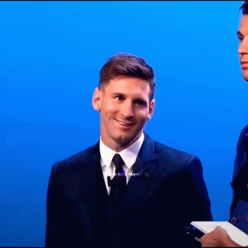 A Man In A Suit And Tie Stands In Front Of A Blue Wall GIF
