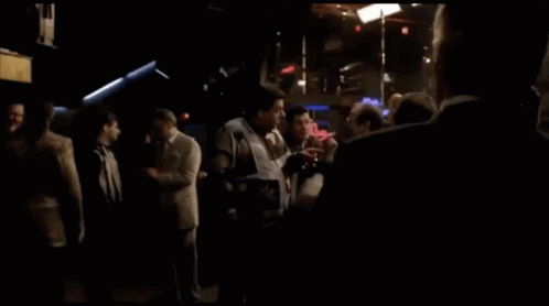 A Man In A Suit And Tie Stands In Front Of A Budweiser Sign GIF