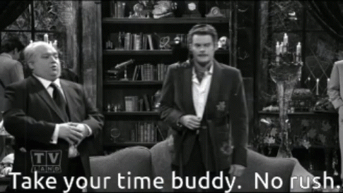 A Man In A Suit And Tie Stands In Front Of A Couch With The Words Take Your Time Buddy No Rush Below Him GIF