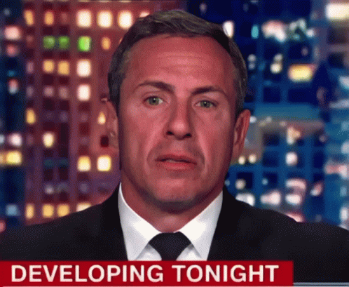 A Man In A Suit And Tie Stands In Front Of A Developing Tonight Sign GIF