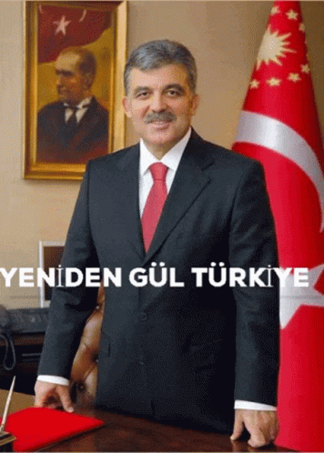 a man in a suit and tie stands in front of a flag with the words yeniden gul turkey written below him