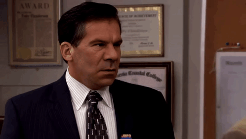 A Man In A Suit And Tie Stands In Front Of A Framed Award GIF