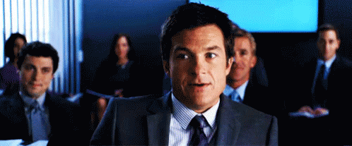 A Man In A Suit And Tie Stands In Front Of A Group Of People In Suits And Ties GIF