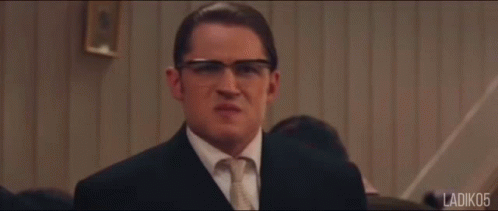 A Man In A Suit And Tie Stands In Front Of A Group Of People With Ladiko5 Written In The Corner GIF