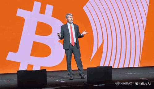 a man in a suit and tie stands in front of a large b on a stage