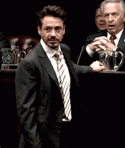 A Man In A Suit And Tie Stands In Front Of A Microphone GIF