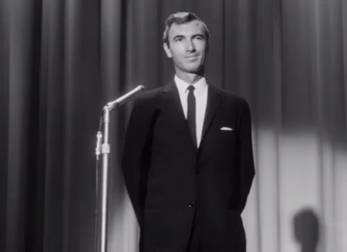 A Man In A Suit And Tie Stands In Front Of A Microphone On A Stage GIF