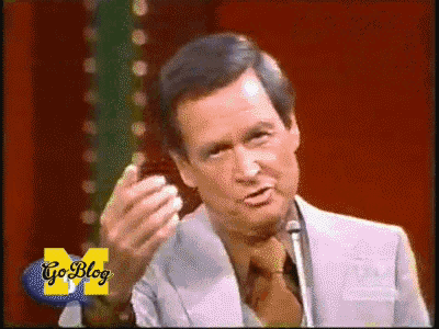 a man in a suit and tie stands in front of a microphone with go blog written on the bottom right