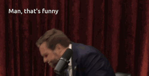 A Man In A Suit And Tie Stands In Front Of A Microphone With The Caption Man That 'S Funny GIF
