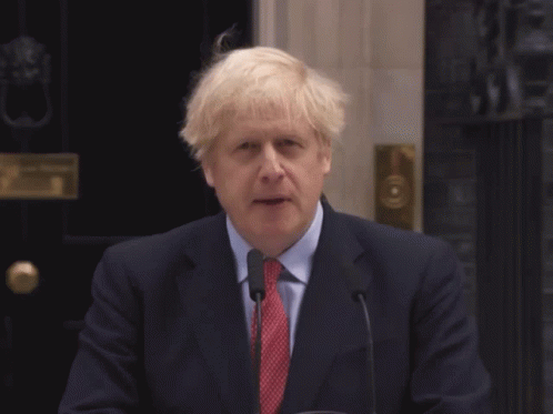 A Man In A Suit And Tie Stands In Front Of A Microphone With The Words An Unexpected Written Below Him GIF