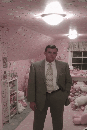 A Man In A Suit And Tie Stands In Front Of A Pink Hello Kitty Room GIF