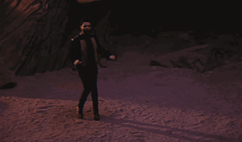 A Man In A Suit And Tie Stands In Front Of A Rock Formation GIF