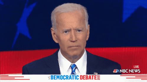 a man in a suit and tie stands in front of a screen that says democratic debate on it