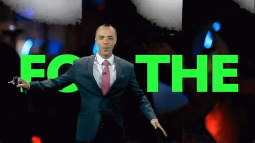 A Man In A Suit And Tie Stands In Front Of A Screen That Says Om 3 GIF