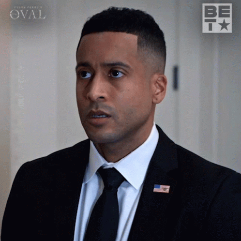 Man In Suit And Tie Standing In Front Of Be Sign GIF