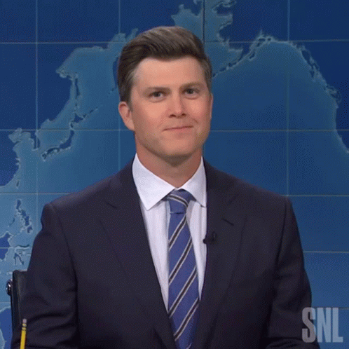 A Man In A Suit And Tie Stands In Front Of A Snl Poster GIF