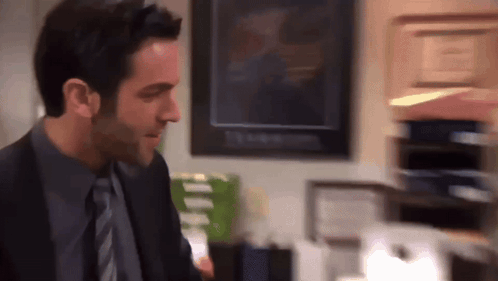 A Man In A Suit And Tie Stands In Front Of A Stack Of Papers GIF