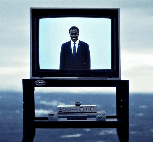a man in a suit and tie stands in front of a television that says lumin on it