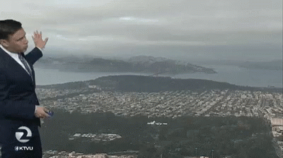 A Man In A Suit And Tie Stands In Front Of A View Of A City And Mountains With The Number 2 On His Shirt GIF
