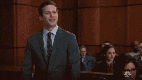 A Man In A Suit And Tie Stands In Front Of A Wall That Says Cool On It GIF