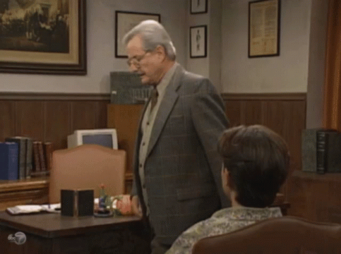 A Man In A Suit And Tie Stands In Front Of A Woman In A Chair With The Words Let Me Show You My Big GIF