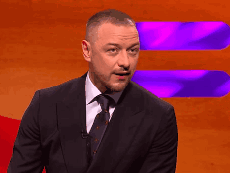 A Man In A Suit And Tie Stands In Front Of An Orange And Purple Background GIF