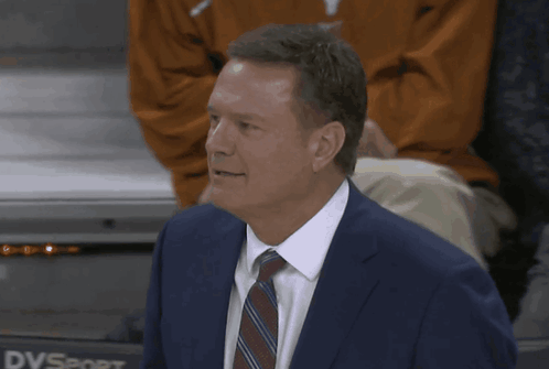 A Man In A Suit And Tie Stands In Front Of Dvsport GIF