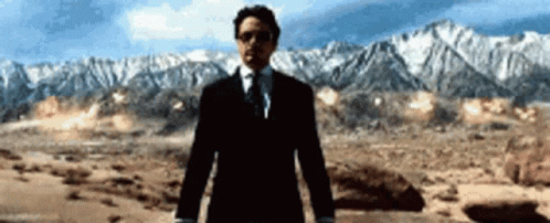 A Man In A Suit And Tie Stands In Front Of Mountains GIF