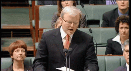 A Man In A Suit And Tie Stands In Front Of Two Microphones GIF