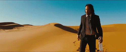 A Man In A Suit And Tie Stands In The Desert Holding A Bottle GIF