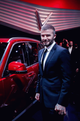 A Man In A Suit And Tie Stands Next To A Red Car GIF