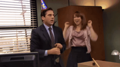 A Man In A Suit And Tie Stands Next To A Woman In A Pink Shirt GIF