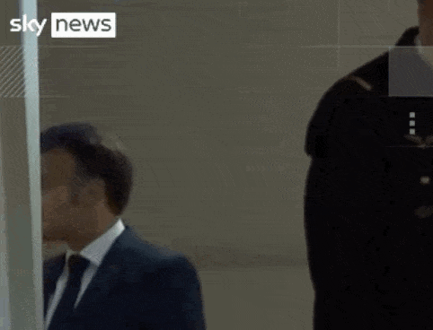 a man in a suit and tie stands next to a woman in a yellow vest that says sky news