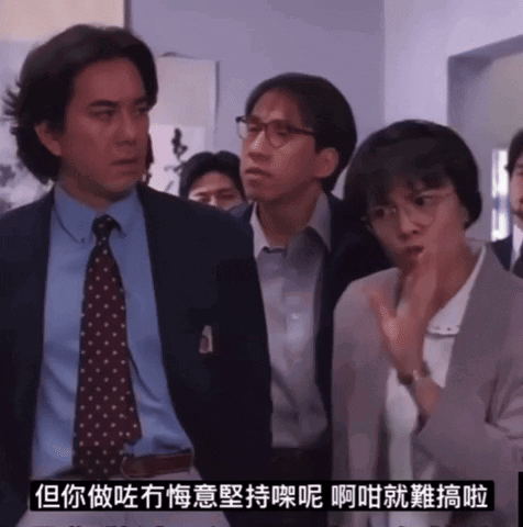 A Man In A Suit And Tie Stands Next To A Woman In Glasses GIF
