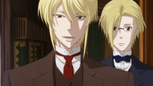 A Man In A Suit And Tie Stands Next To Another Man In A Tuxedo GIF