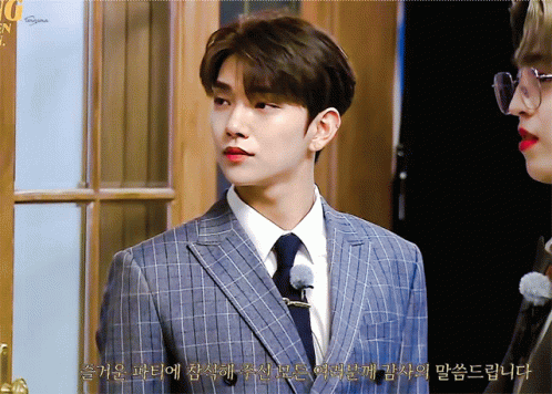 A Man In A Suit And Tie Stands Next To Another Man In Glasses And Red Lipstick GIF