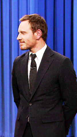 A Man In A Suit And Tie Stands With His Hands Behind His Back GIF