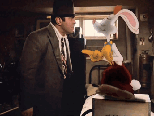 A Man In A Suit And Tie Talks To A Cartoon Rabbit Wearing A Santa Hat GIF