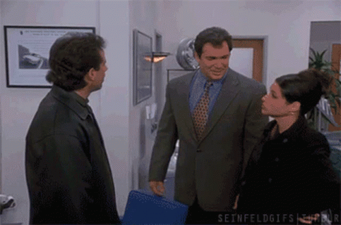 A Man In A Suit And Tie Talks To A Woman In A Black Jacket GIF