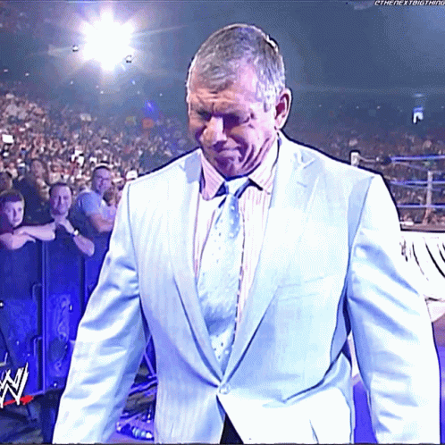 A Man In A Suit And Tie Walks Into A Wrestling Ring With The Letters W On The Bottom Right GIF
