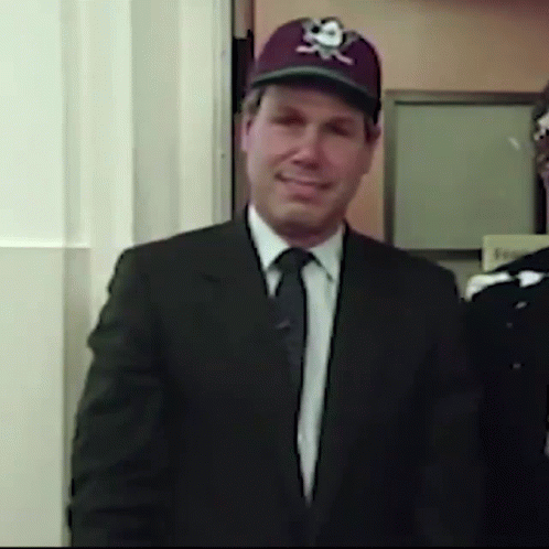 A Man In A Suit And Tie Wearing A Baseball Cap With A Skull And Crossbones On It GIF